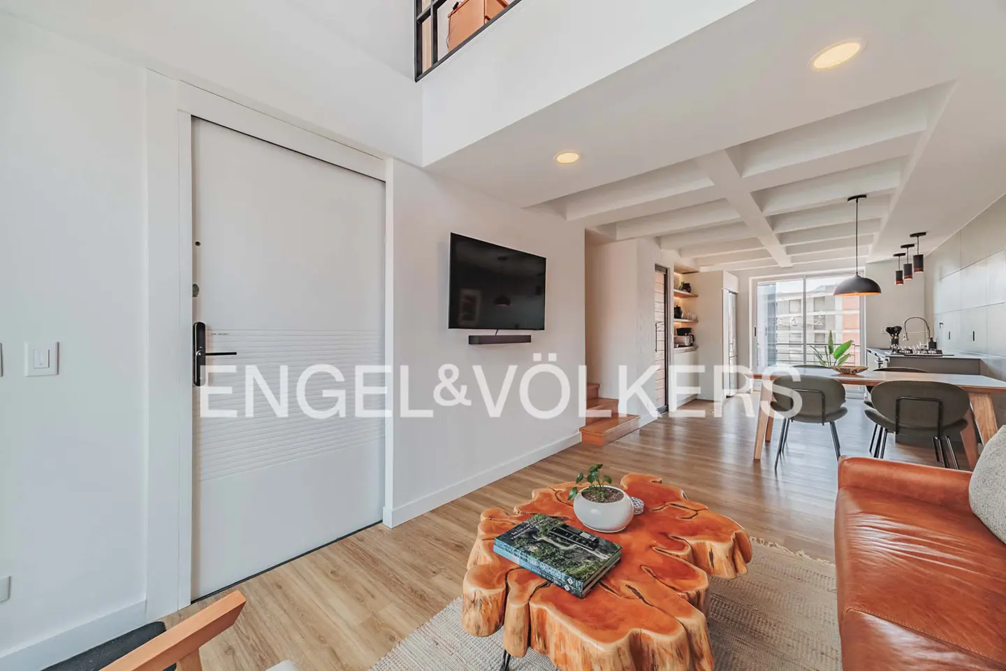 Bright, modern living space with a wood coffee table, leather couch, and TV. The Engel & Völkers logo is visible.