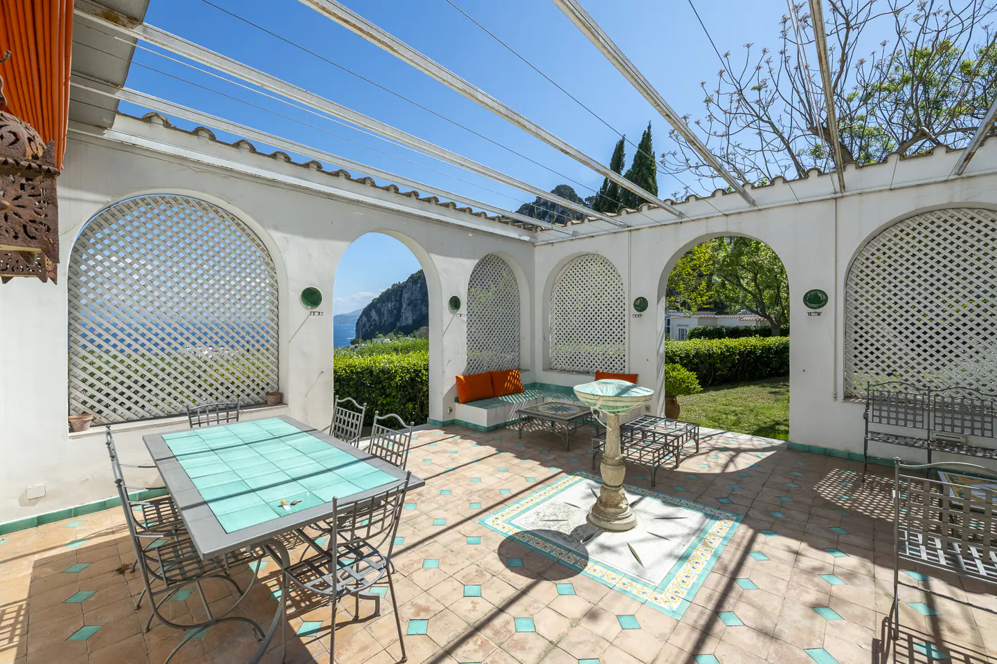 Outdoor patio with white arches, a turquoise table, and a view of the sea and mountains.