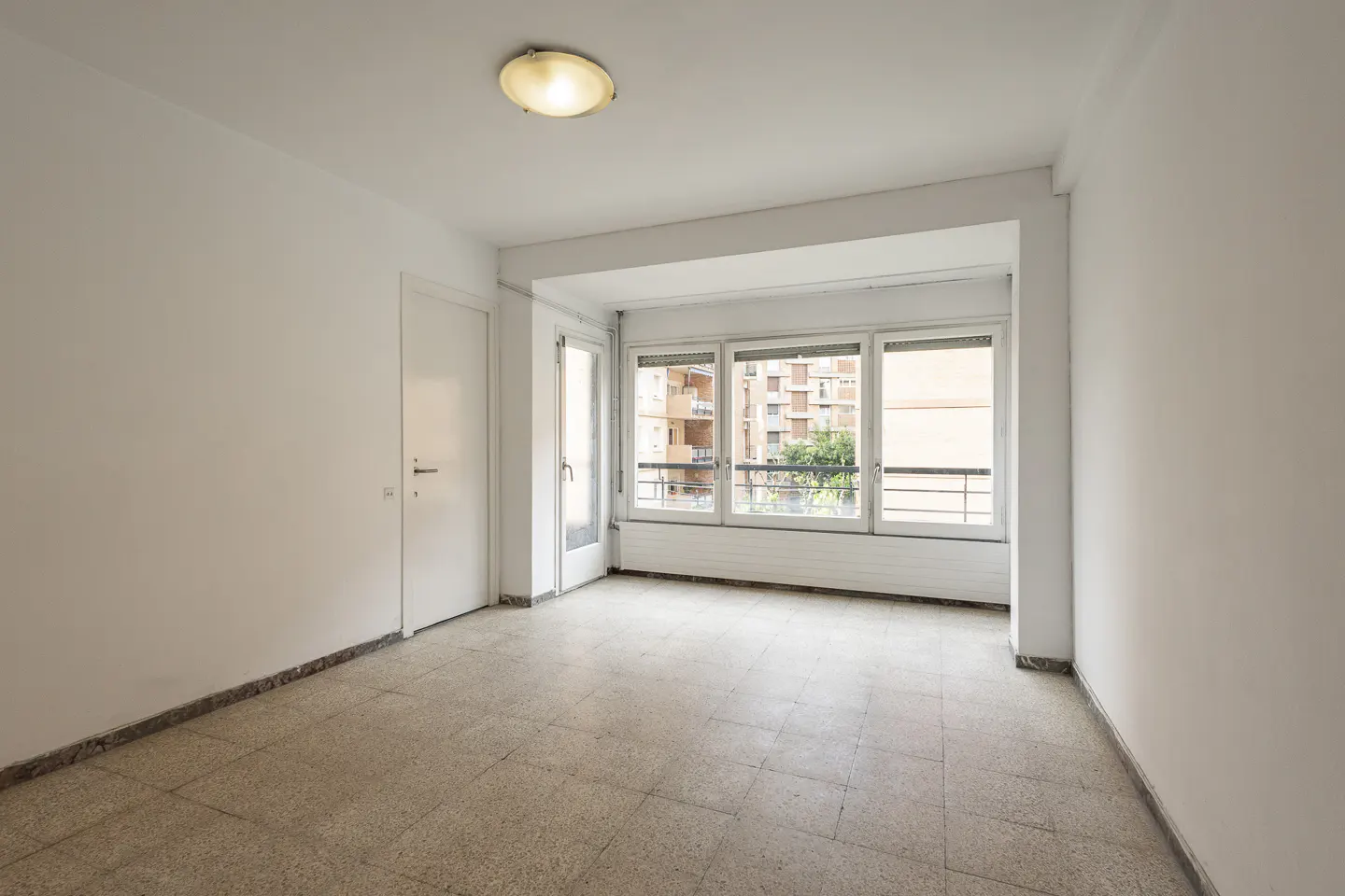 Empty room with white walls, tiled floor, and a window showing an apartment building.