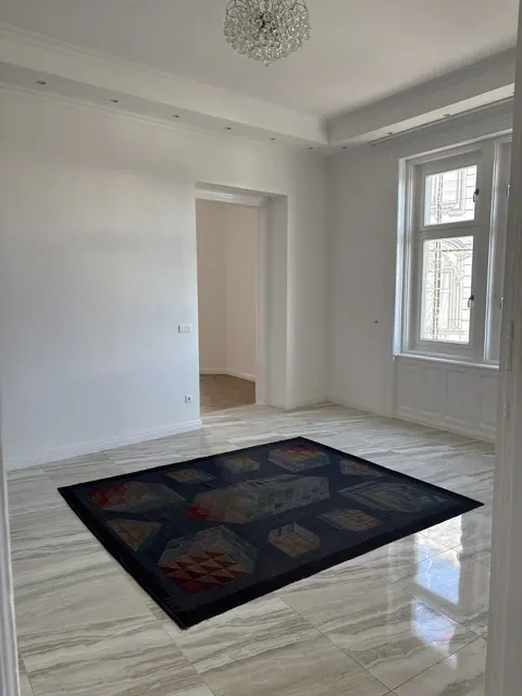 Bright, empty room with white walls, marble floors, and a dark rug. A window and doorway are visible.