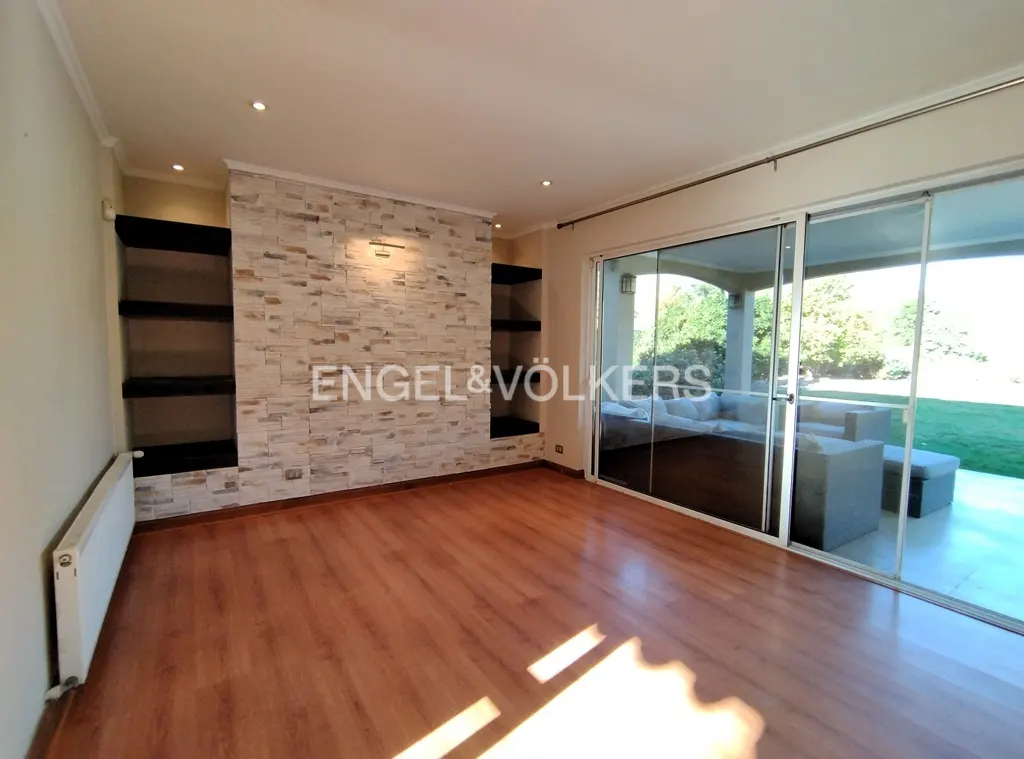 An empty living room with wood floors, a stone accent wall with shelves, and sliding glass doors to a patio.