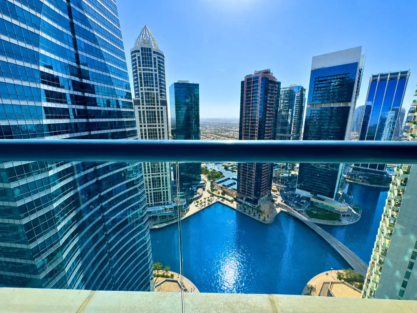 View from a high-rise balcony overlooking blue waterways and modern skyscrapers on a sunny day.