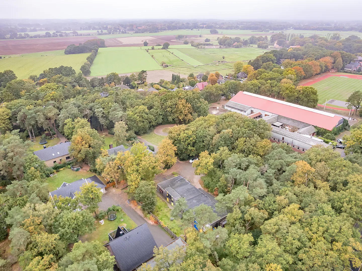 Aerial view of a property with houses, a barn with a red roof, and green fields in the background.
