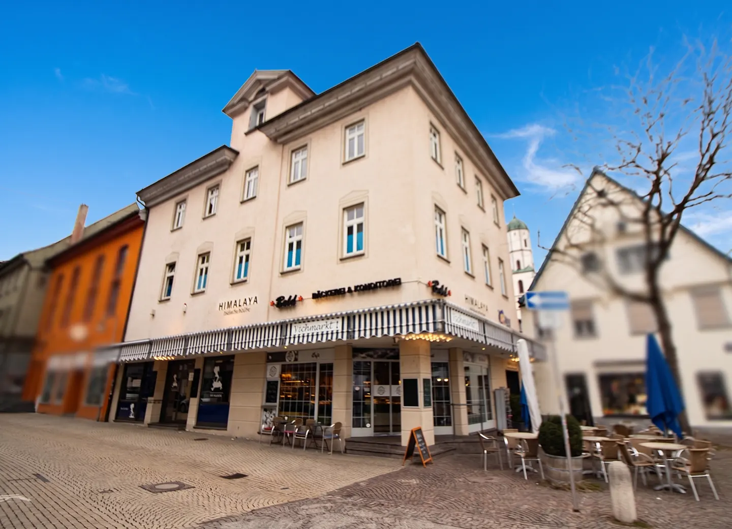 Exterior view of a three-story building with a bakery and cafe on the ground floor. Tables and chairs are set up outside.