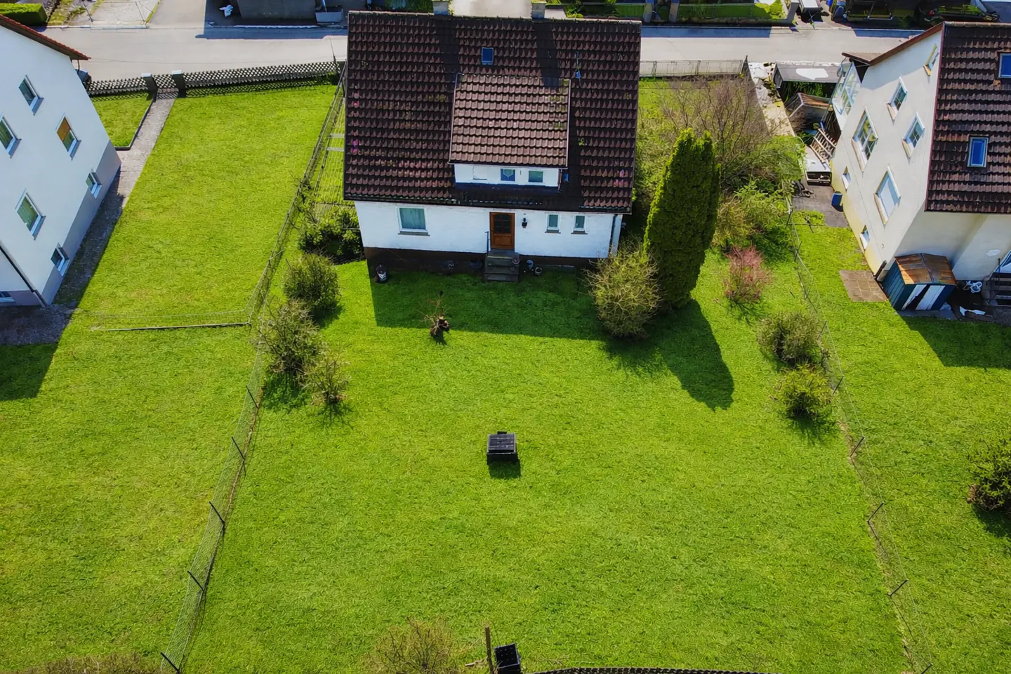Aerial view of a white house with a brown roof, surrounded by a large green lawn and neighboring houses.
