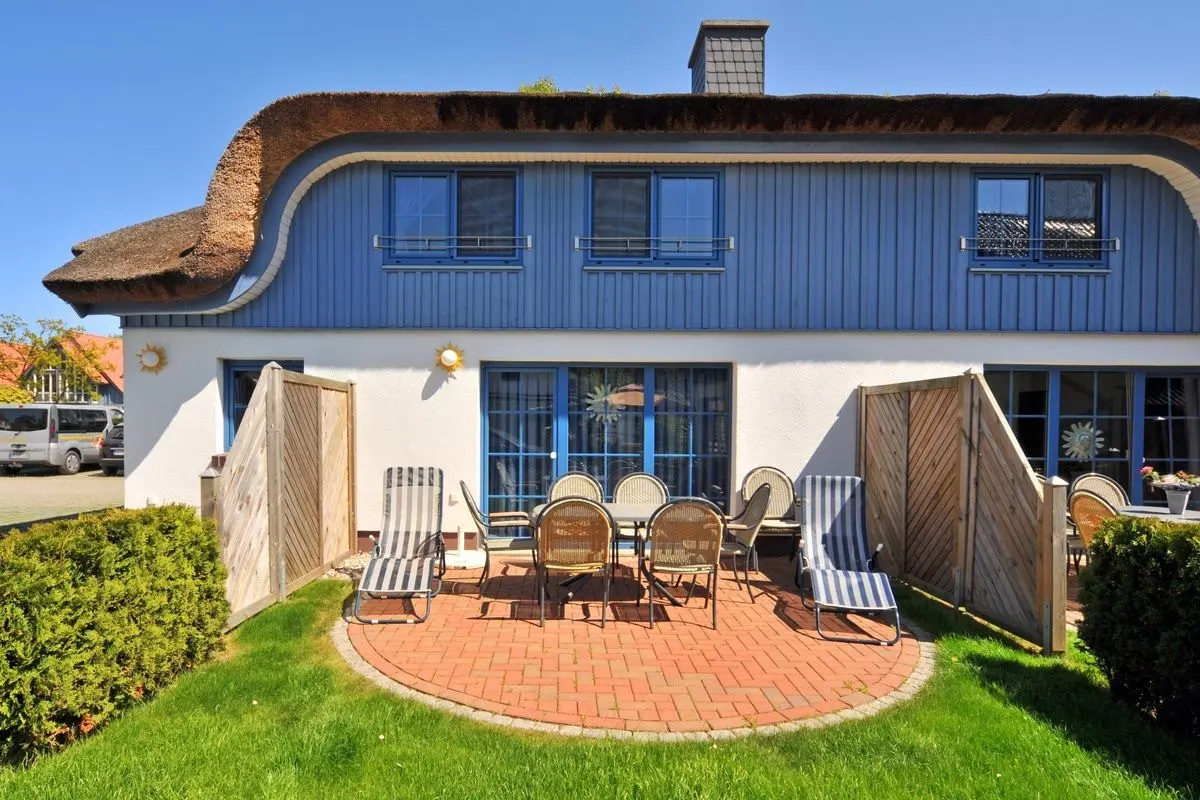 Exterior of a blue and white house with a thatched roof and a brick patio with outdoor furniture.
