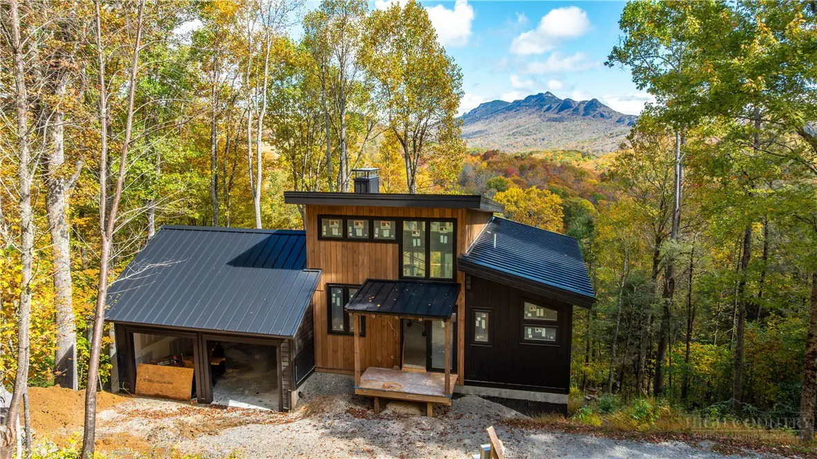 Modern wood and black home with a metal roof, surrounded by fall foliage and a mountain in the background.