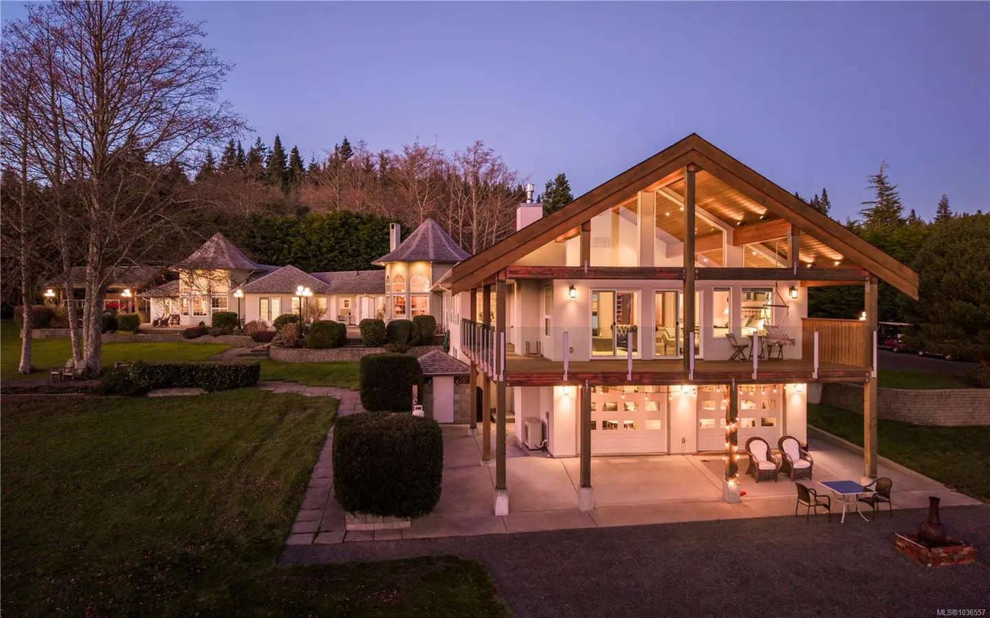 Two-story house with a wood frame and white walls, a deck, and a garage with string lights. A lawn and trees surround the house.