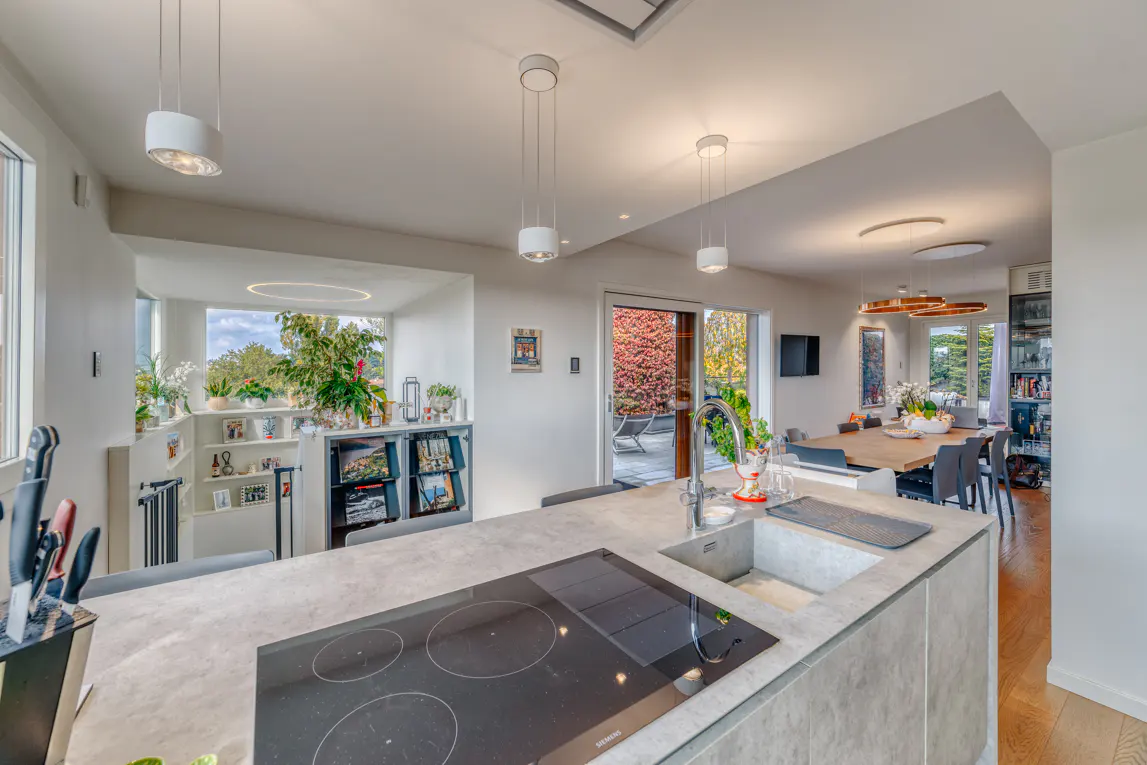 Open-concept kitchen with a gray island, black cooktop, sink, and stainless steel faucet. Dining area and outdoor patio visible in the background.
