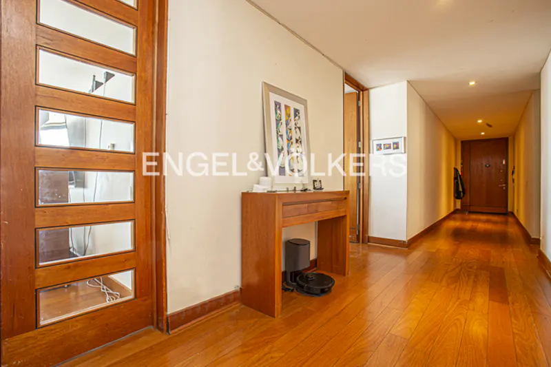 Hallway with wood floors, a console table with a robot vacuum, and a wood door with glass panels.