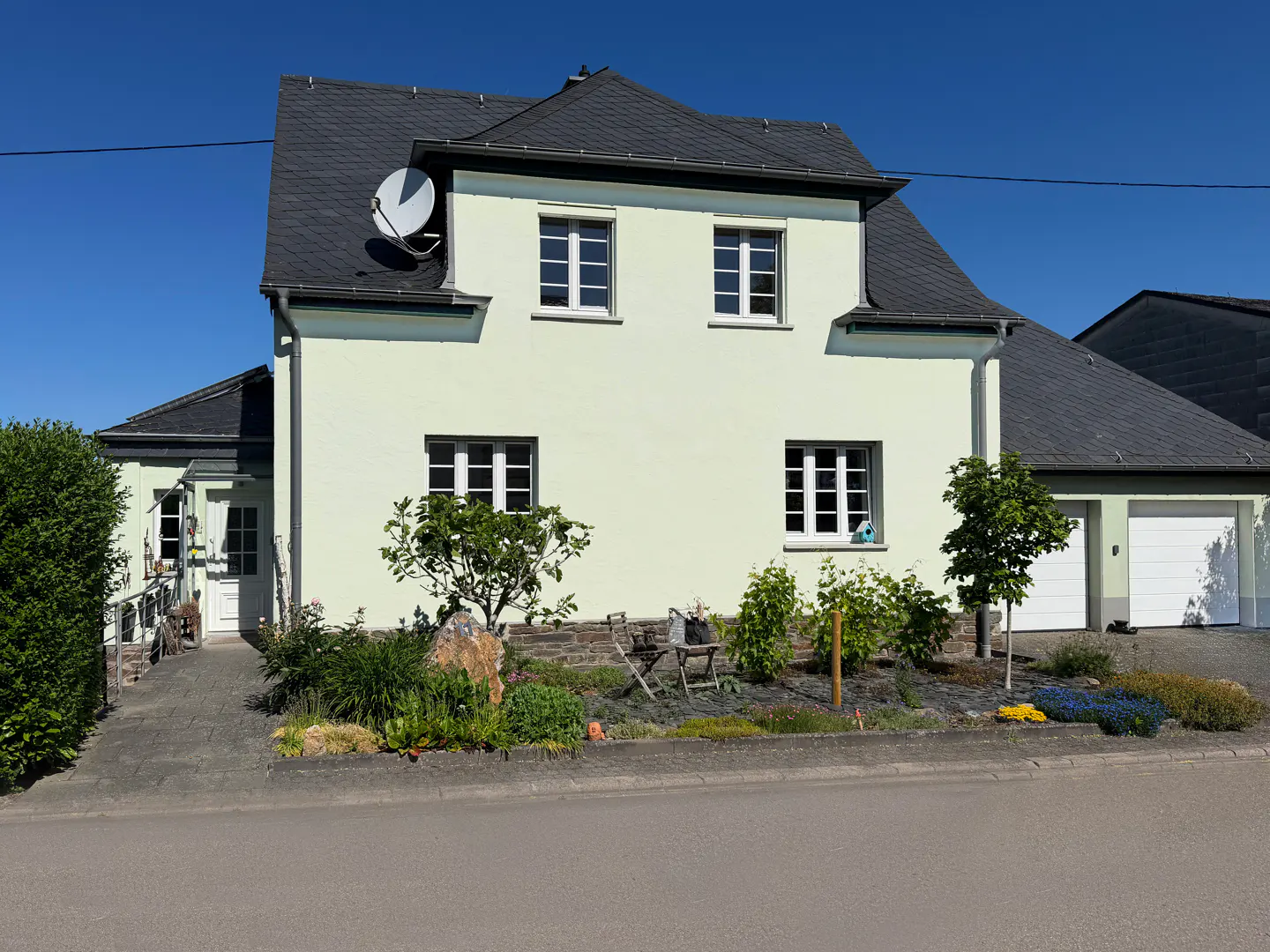 A pale yellow two-story house with a dark slate roof, white trim, and an attached garage under a clear blue sky.