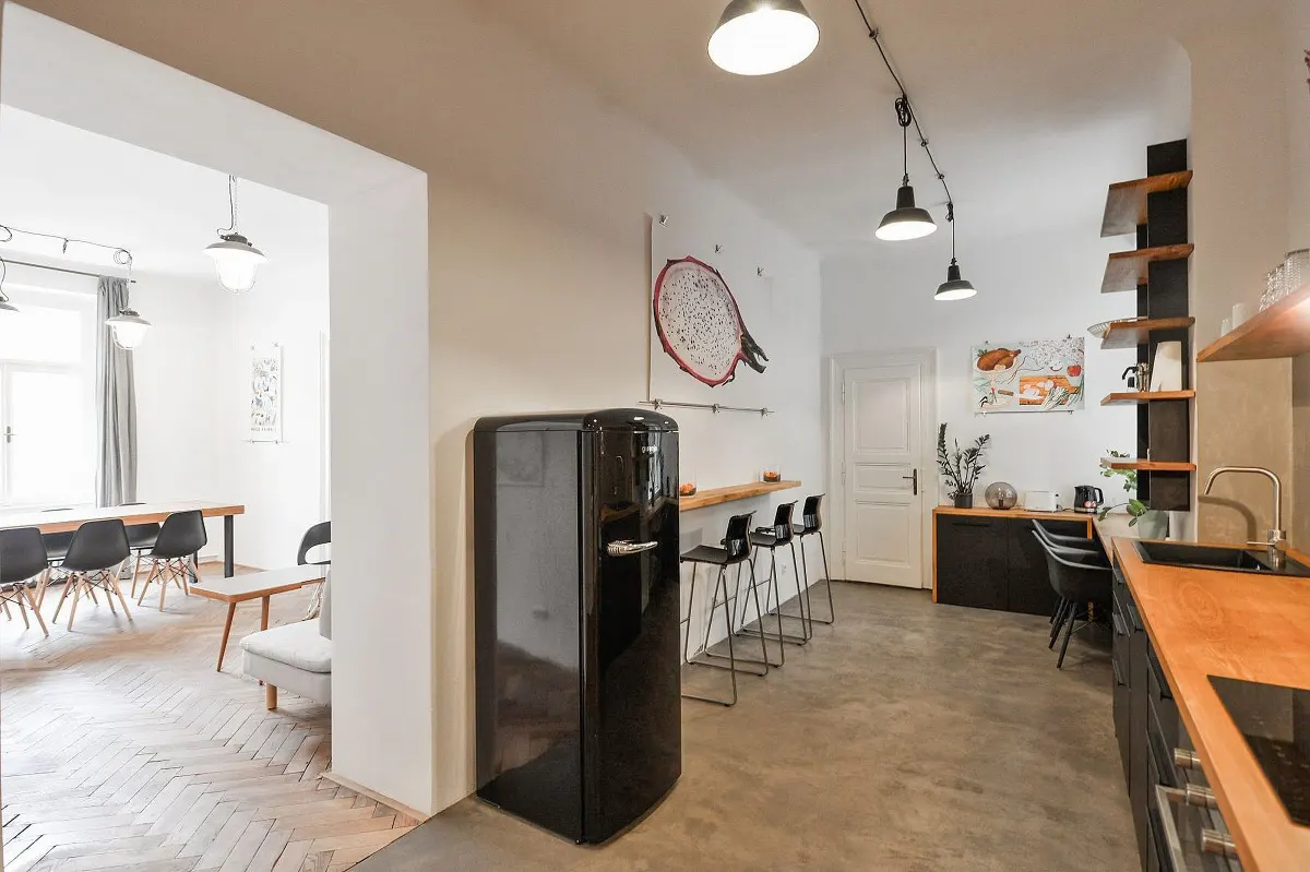 A modern kitchen with a black retro refrigerator, wooden countertops, and a dining area in the background.