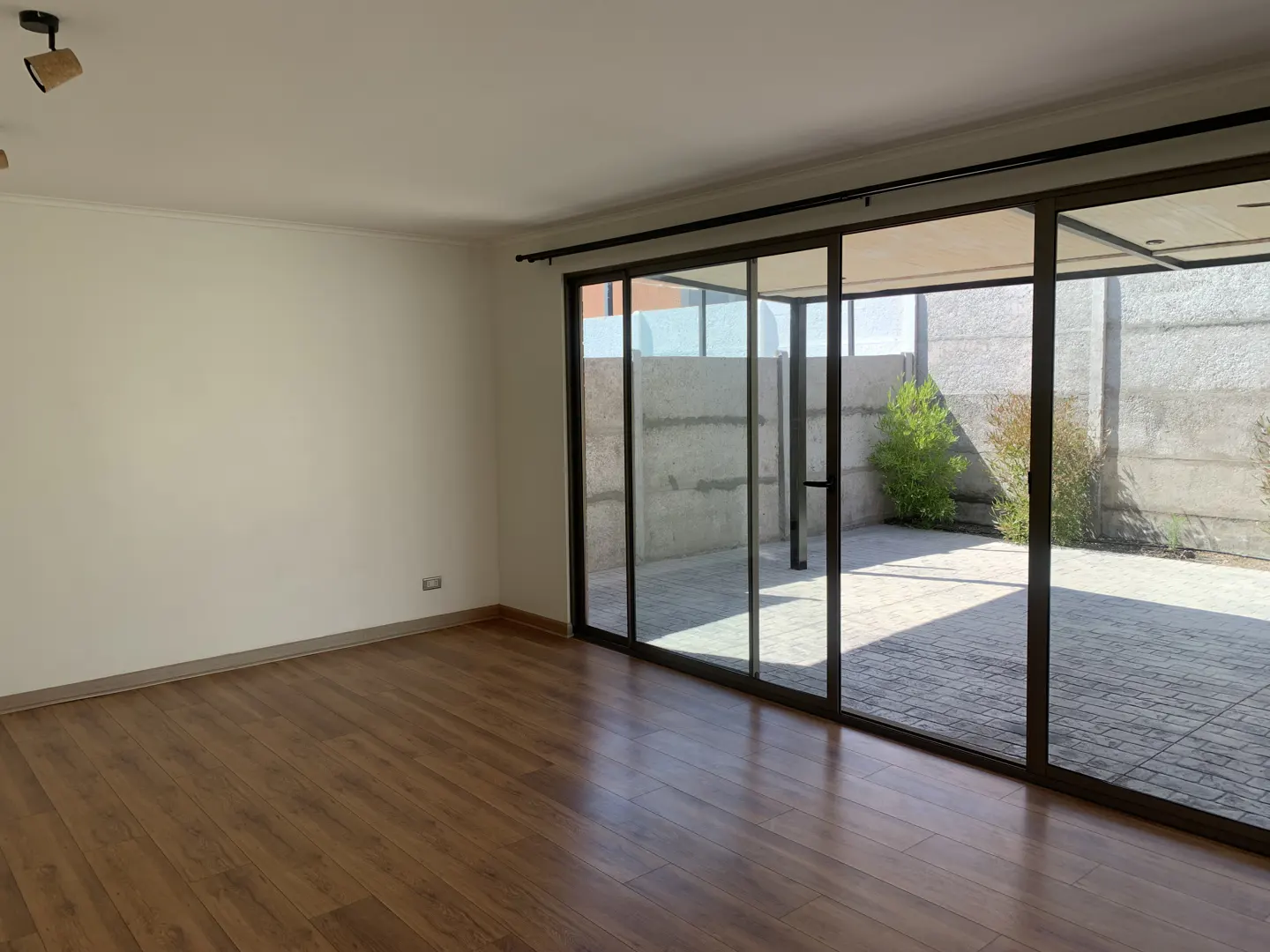 An empty room with wood floors and white walls has large sliding glass doors to a patio.