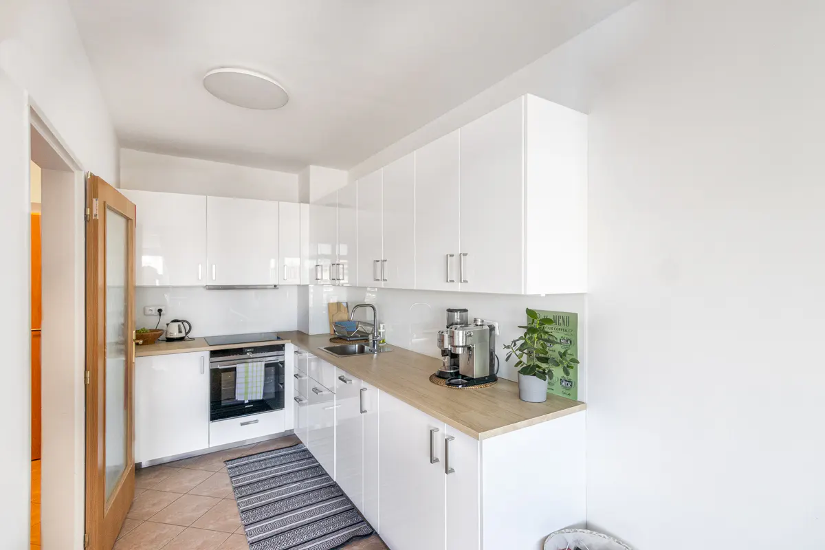 Bright, modern kitchen with white cabinets, wood countertops, and stainless steel appliances. A gray striped rug lies on the tiled floor.