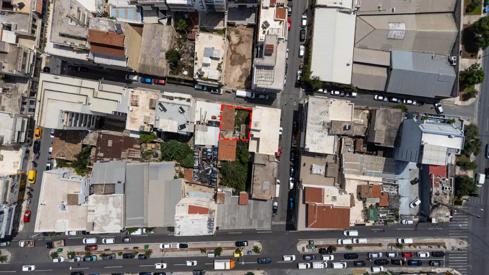 Aerial view of a city block with a red dashed outline highlighting a vacant rectangular plot of land between buildings.