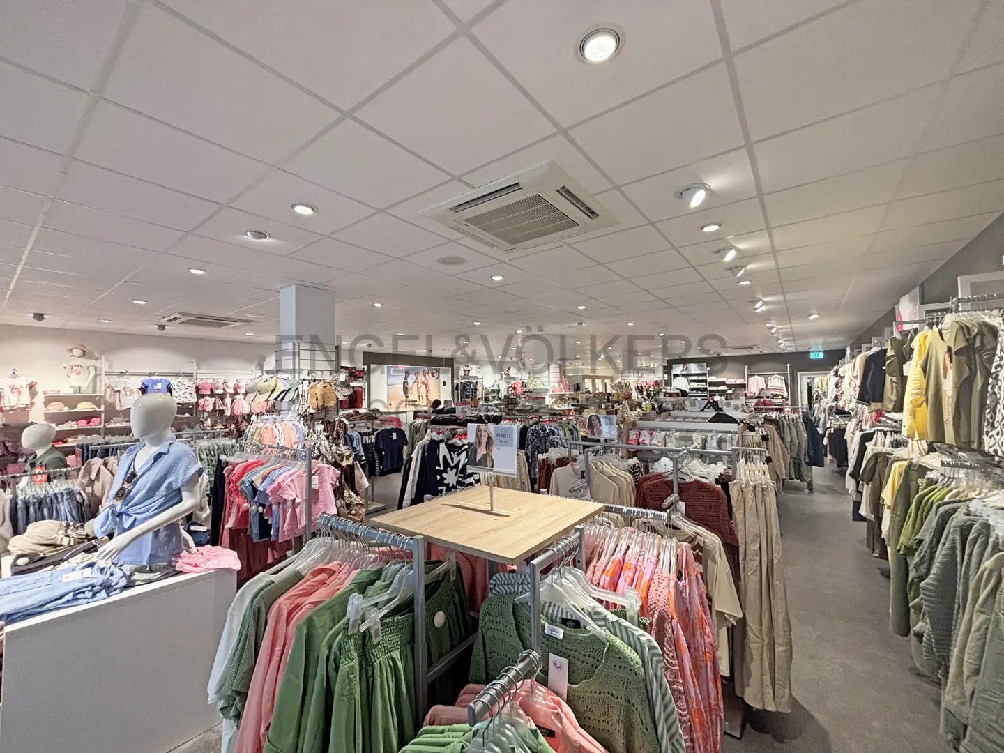 Interior view of a clothing store with racks of colorful clothes and a mannequin in a blue shirt.