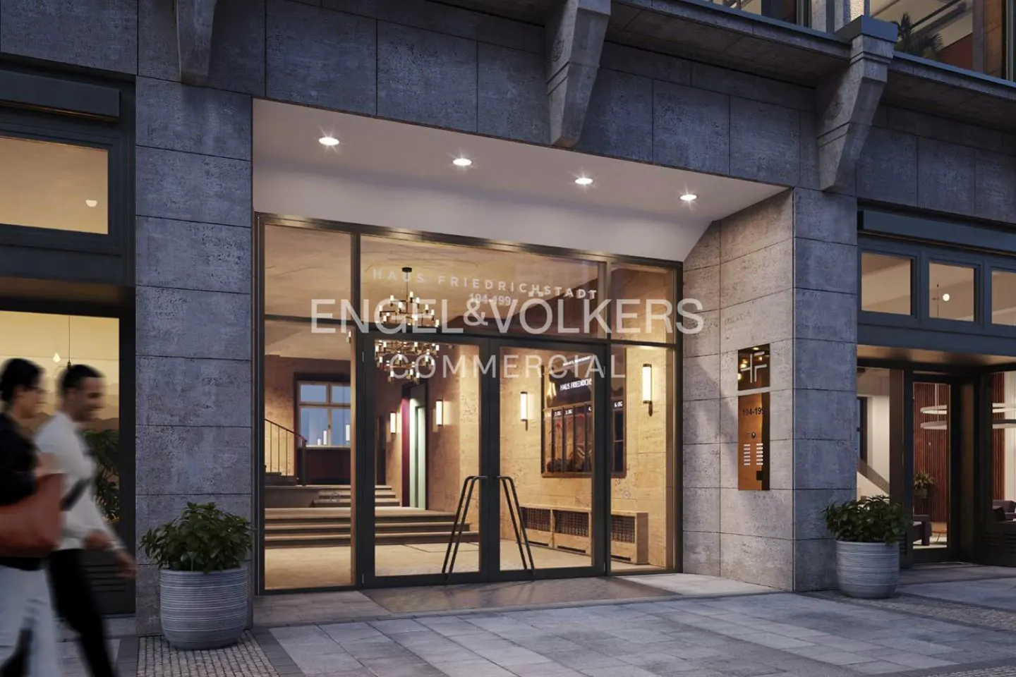 Exterior view of Engel & Volkers Commercial office with glass doors, stone facade, and potted plants. People walk by.