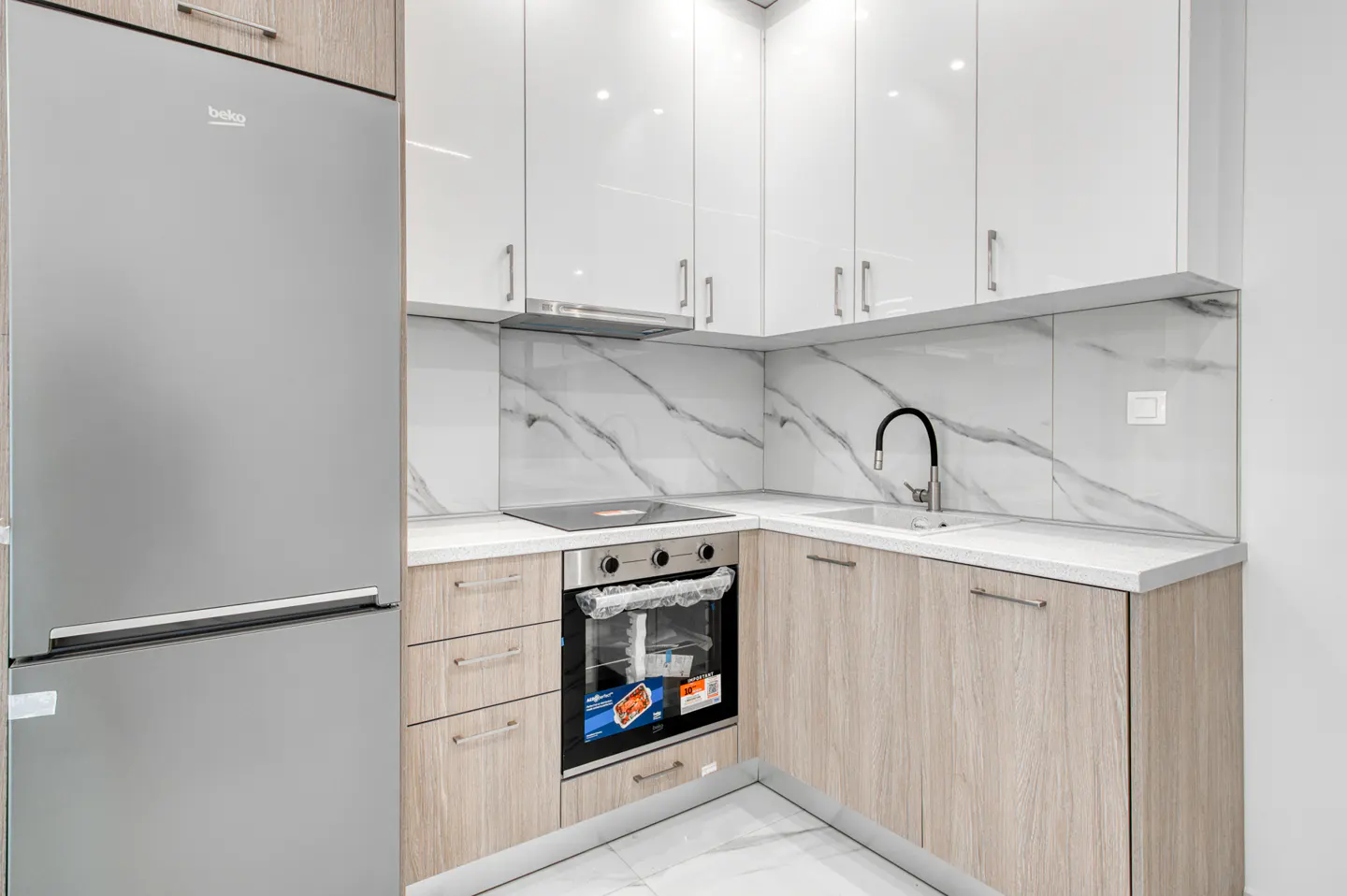 Modern kitchen with white cabinets, marble backsplash, and stainless steel appliances. A gray refrigerator stands to the left of the oven and sink.