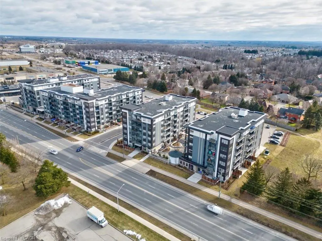 Aerial view of three modern gray apartment buildings along a road with cars, trees, and a cloudy sky.