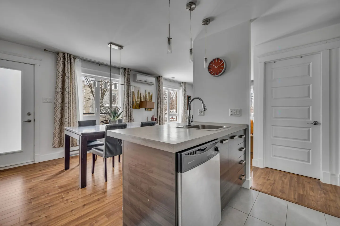 A bright, modern kitchen with a dining area. Features include a kitchen island, stainless steel appliances, and a wooden dining table.