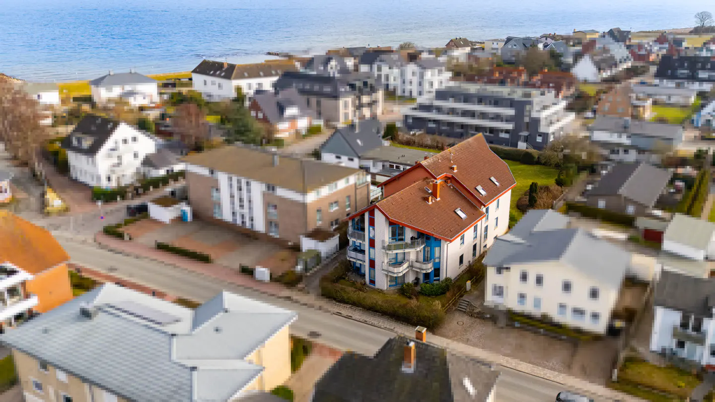 Aerial view of a coastal neighborhood with a white building with a red roof and blue balconies.