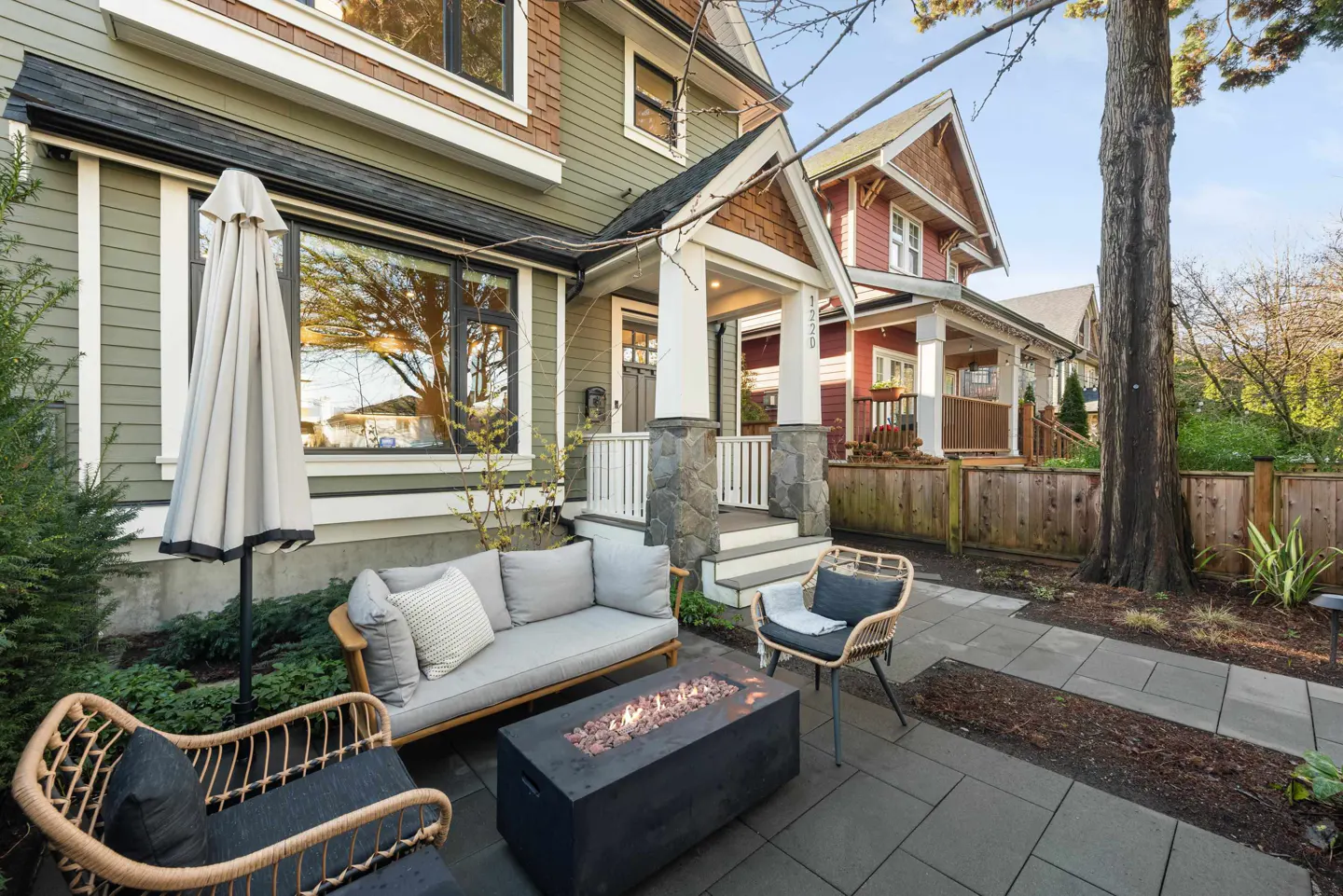 Outdoor patio with a gray sofa, wicker chairs, and a black fire pit. The house is green and brown with a white porch.