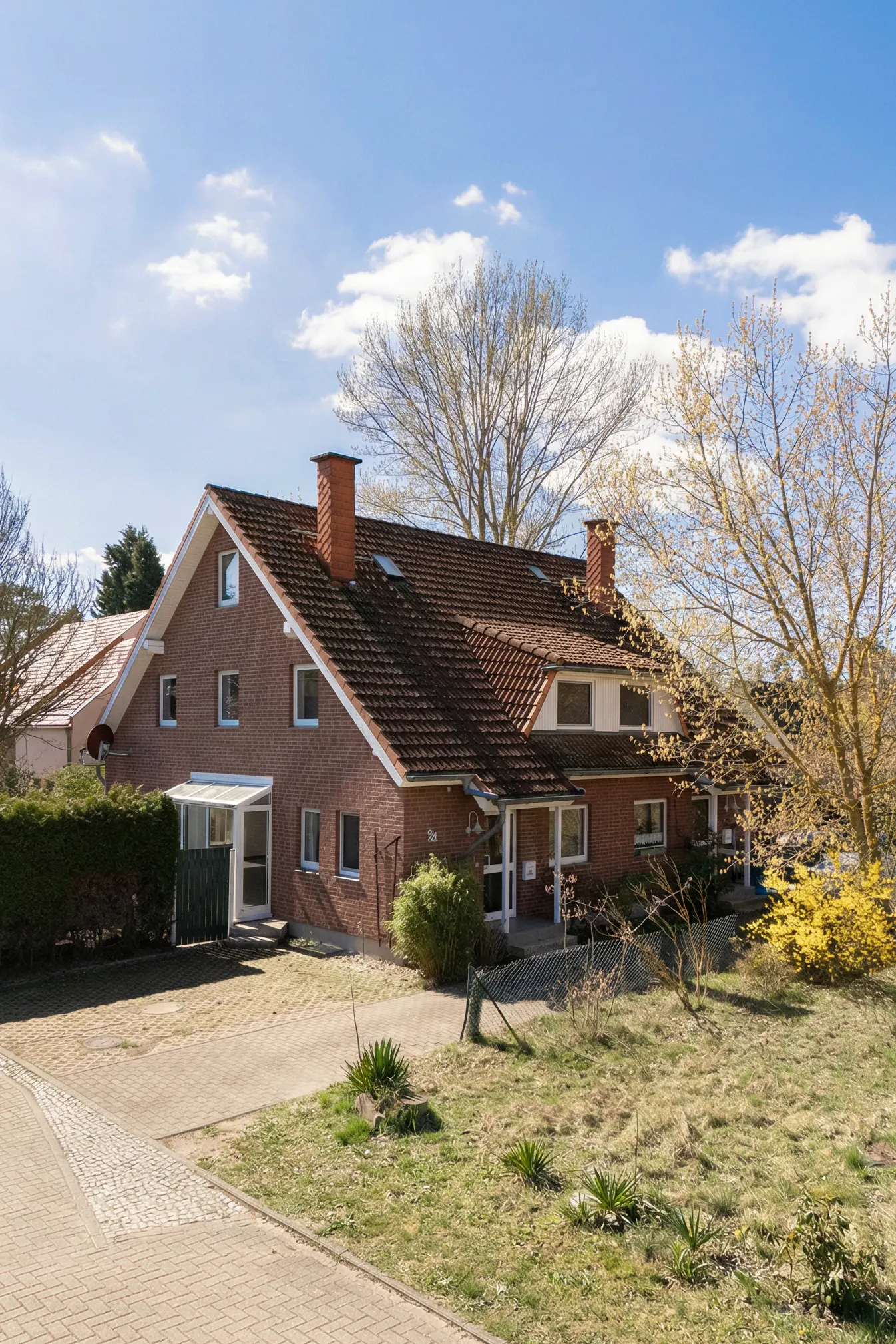 Two-story brick house with a brown roof and two chimneys under a blue sky with trees.