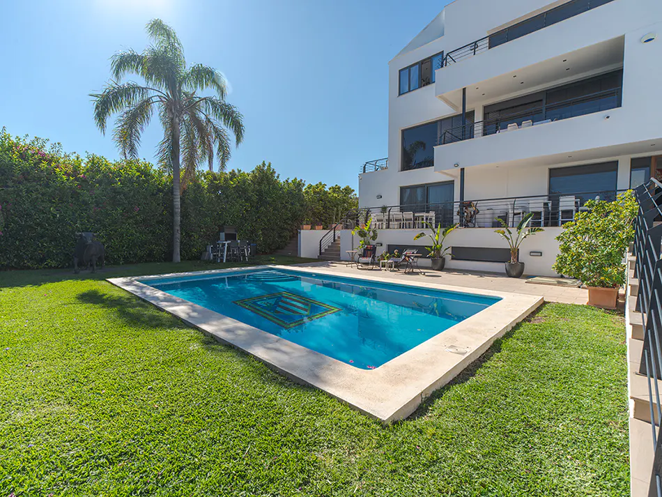 A modern white house with a pool and green lawn on a sunny day.