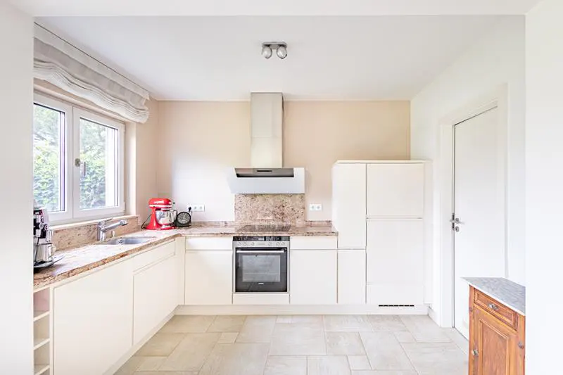 Bright kitchen with white cabinets, granite countertops, and tile floor. A window overlooks greenery. A red stand mixer sits on the counter.