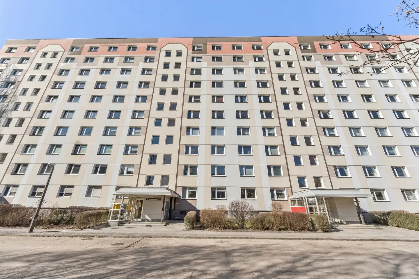 Exterior view of a tall, light beige apartment building with many windows under a clear blue sky.