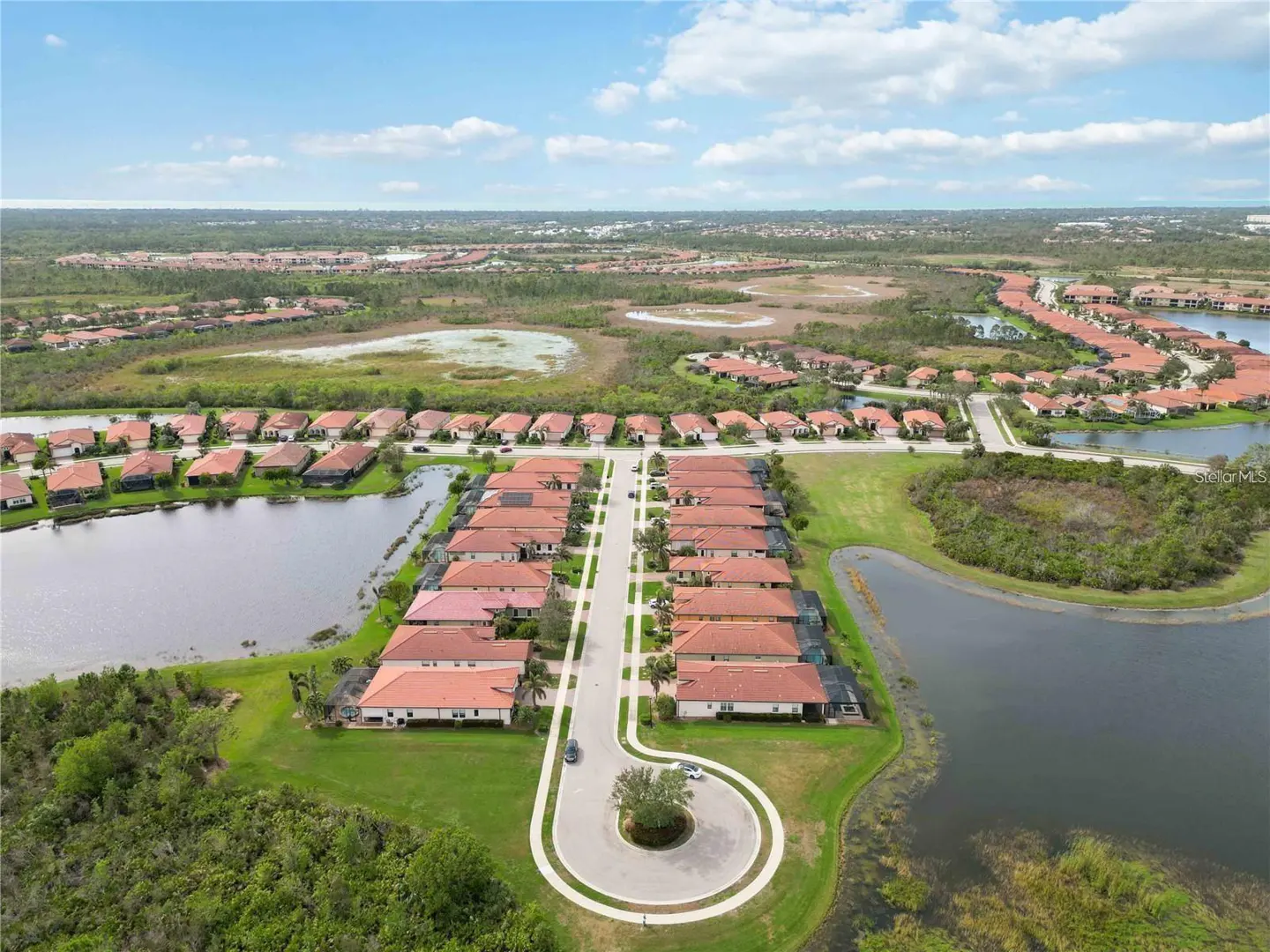 Aerial view of a suburban neighborhood with terracotta-roofed homes, a cul-de-sac, and surrounding lakes and greenery.
