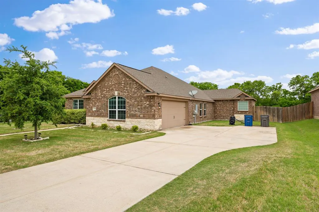 A single-story brick house with a tan garage door and a long concrete driveway on a sunny day.
