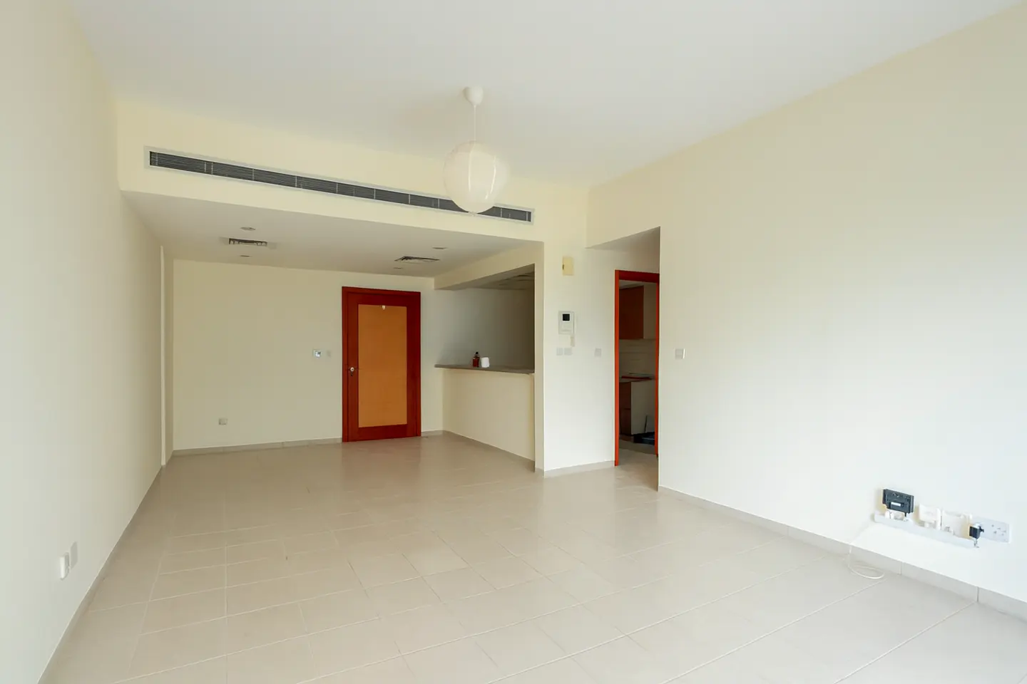 Empty room with beige tile floor, cream walls, and red-framed doors. A white globe light hangs from the ceiling.