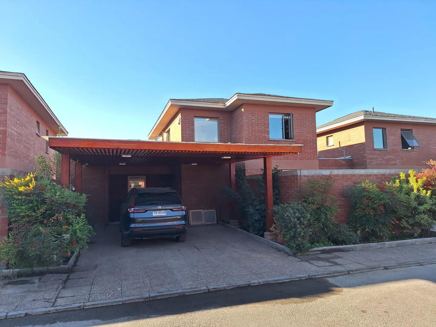 Brick two-story house with a carport and a blue car parked in the driveway on a sunny day.