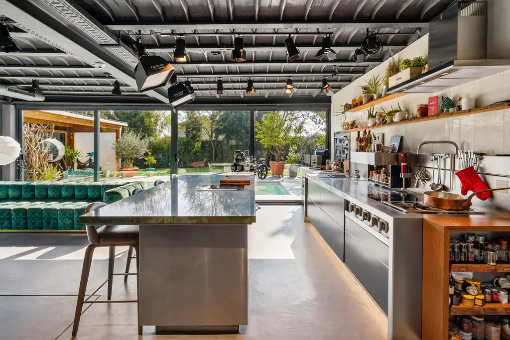 A modern kitchen with stainless steel counters, wood accents, and a large window overlooking a pool and garden.