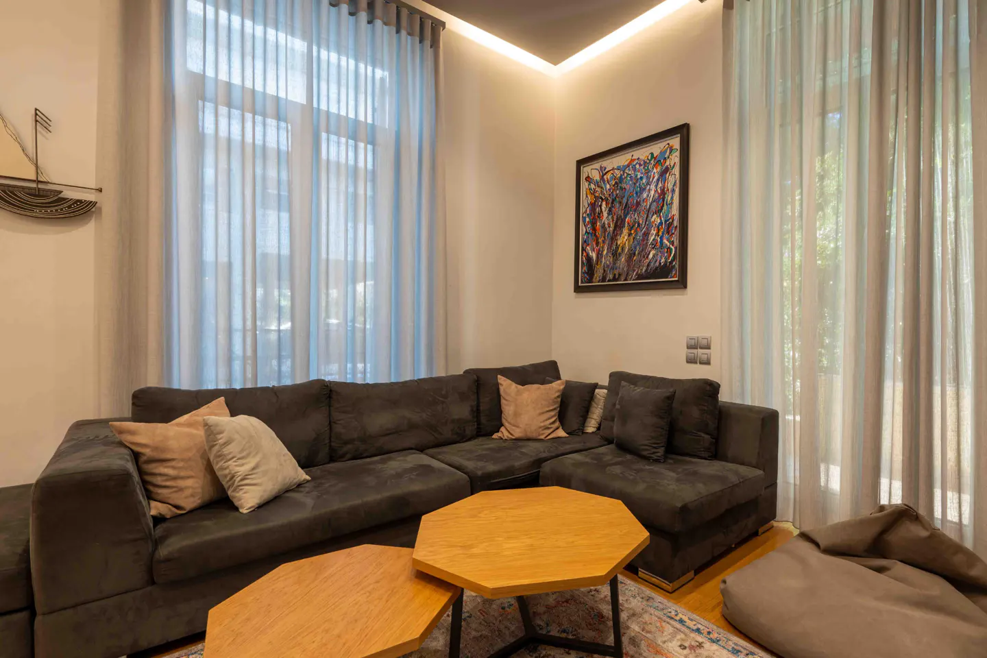 Modern living room with a dark grey sectional sofa, two wooden hexagonal coffee tables, and sheer curtains.