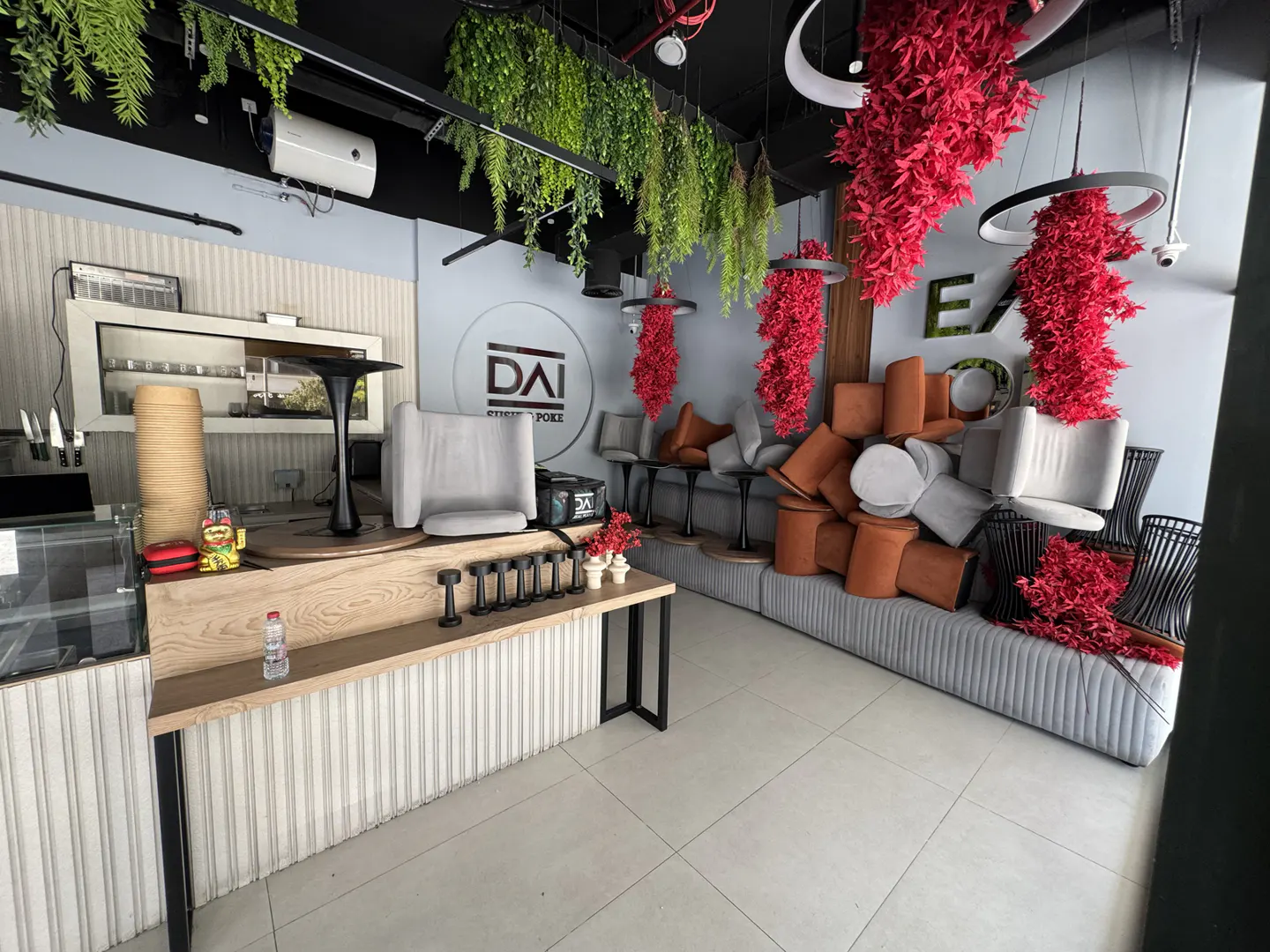 Interior of a restaurant with hanging plants, red floral decorations, and modern furniture. A counter with weights and a water bottle is in the foreground.