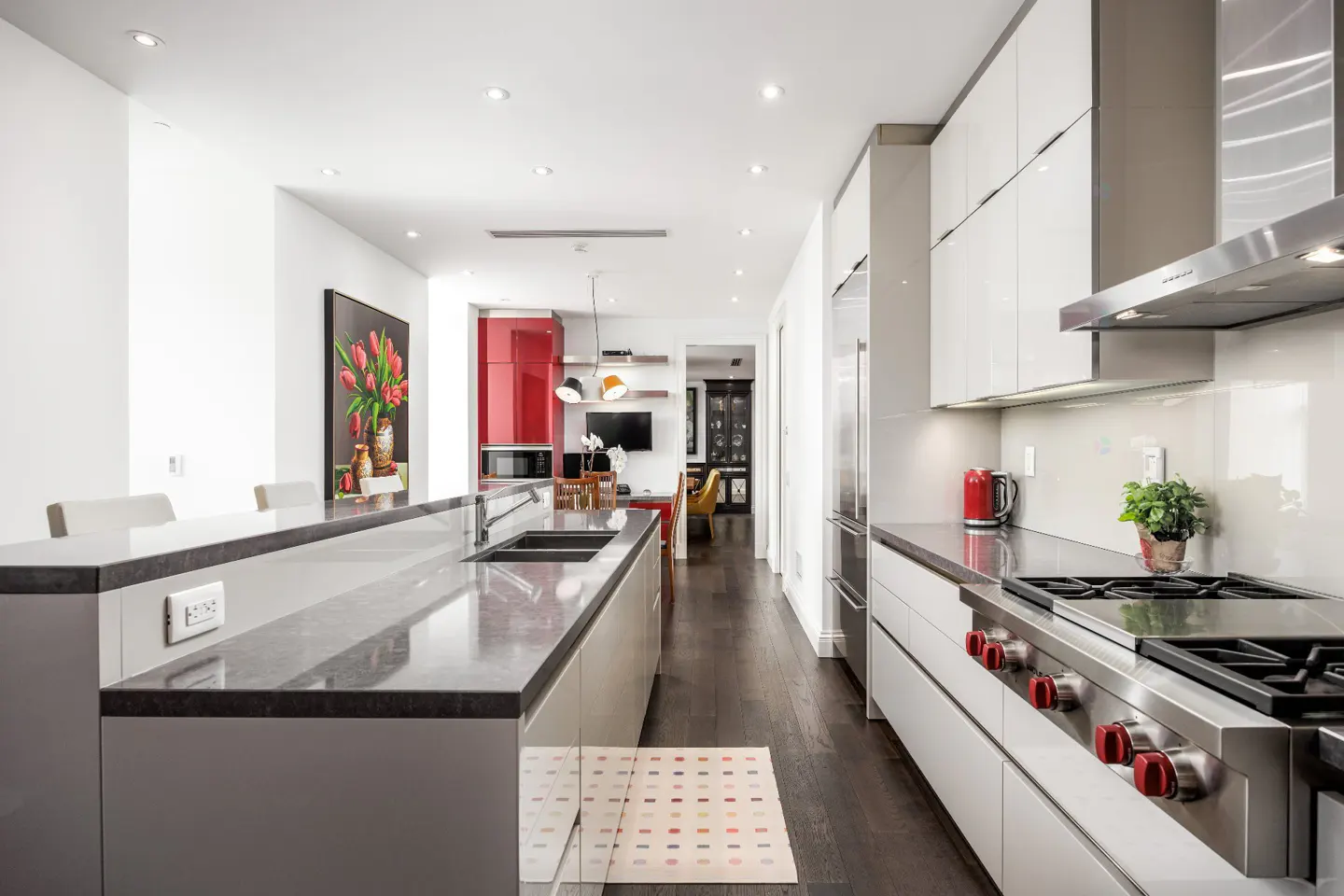 Bright, modern kitchen with a gray island, stainless steel appliances, and white cabinets. A red accent wall and tulip painting add pops of color.