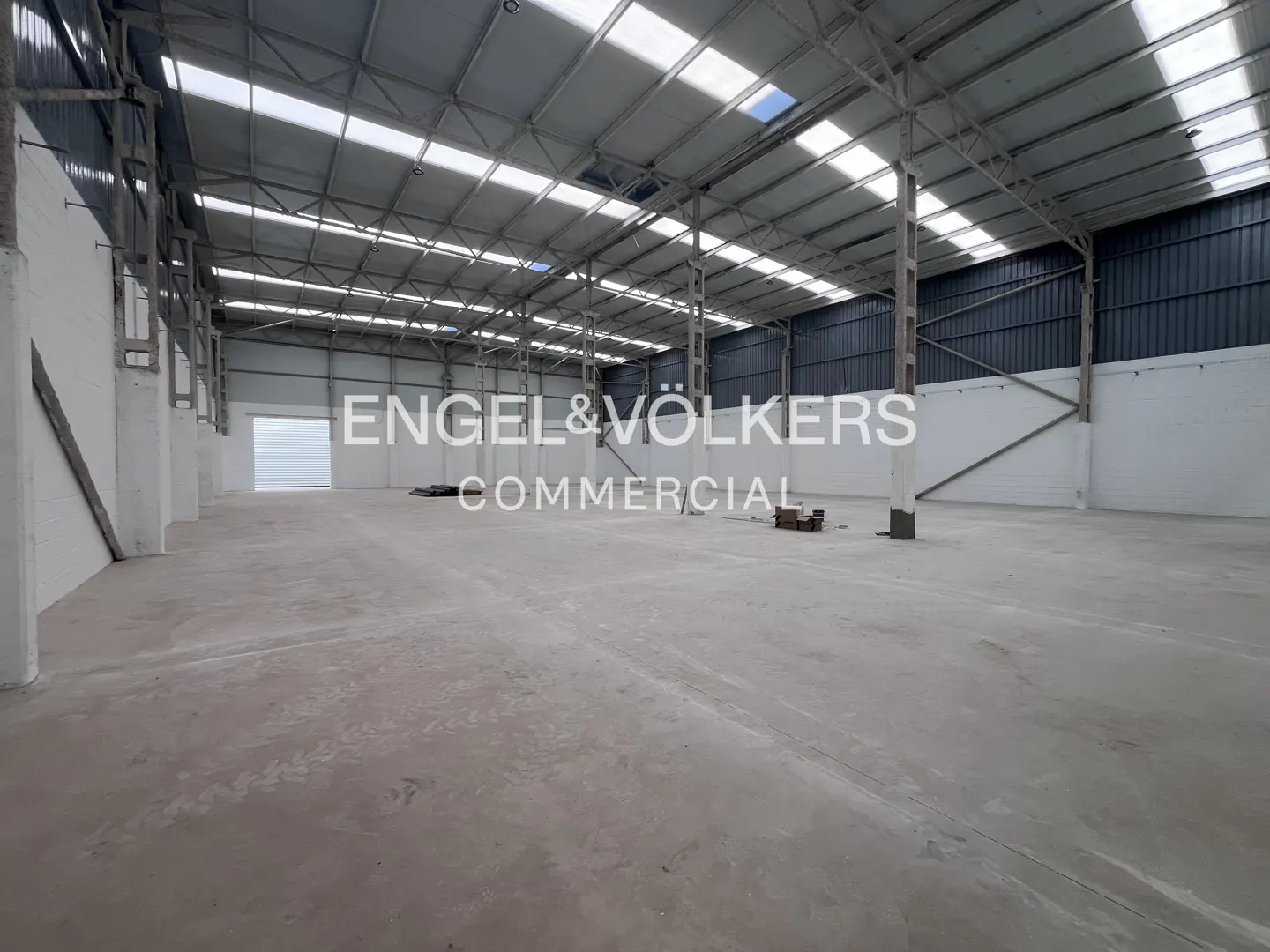 Spacious, empty industrial warehouse with high ceilings, concrete floors, white walls, and skylights.