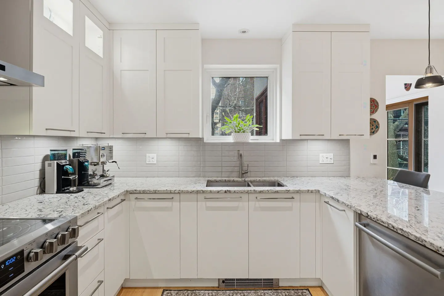 Bright kitchen with white cabinets, granite countertops, and stainless steel appliances. A window above the sink offers natural light.