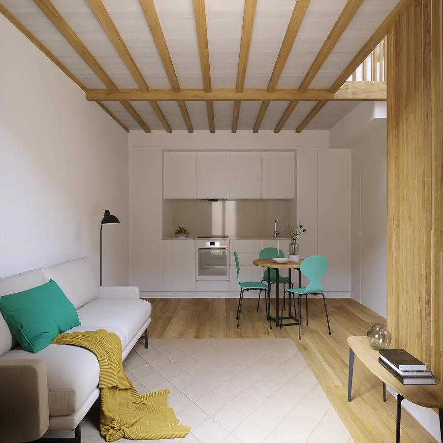 Modern open-plan living area with white kitchen, wooden ceiling beams, white sofa with green pillow, and teal dining chairs.
