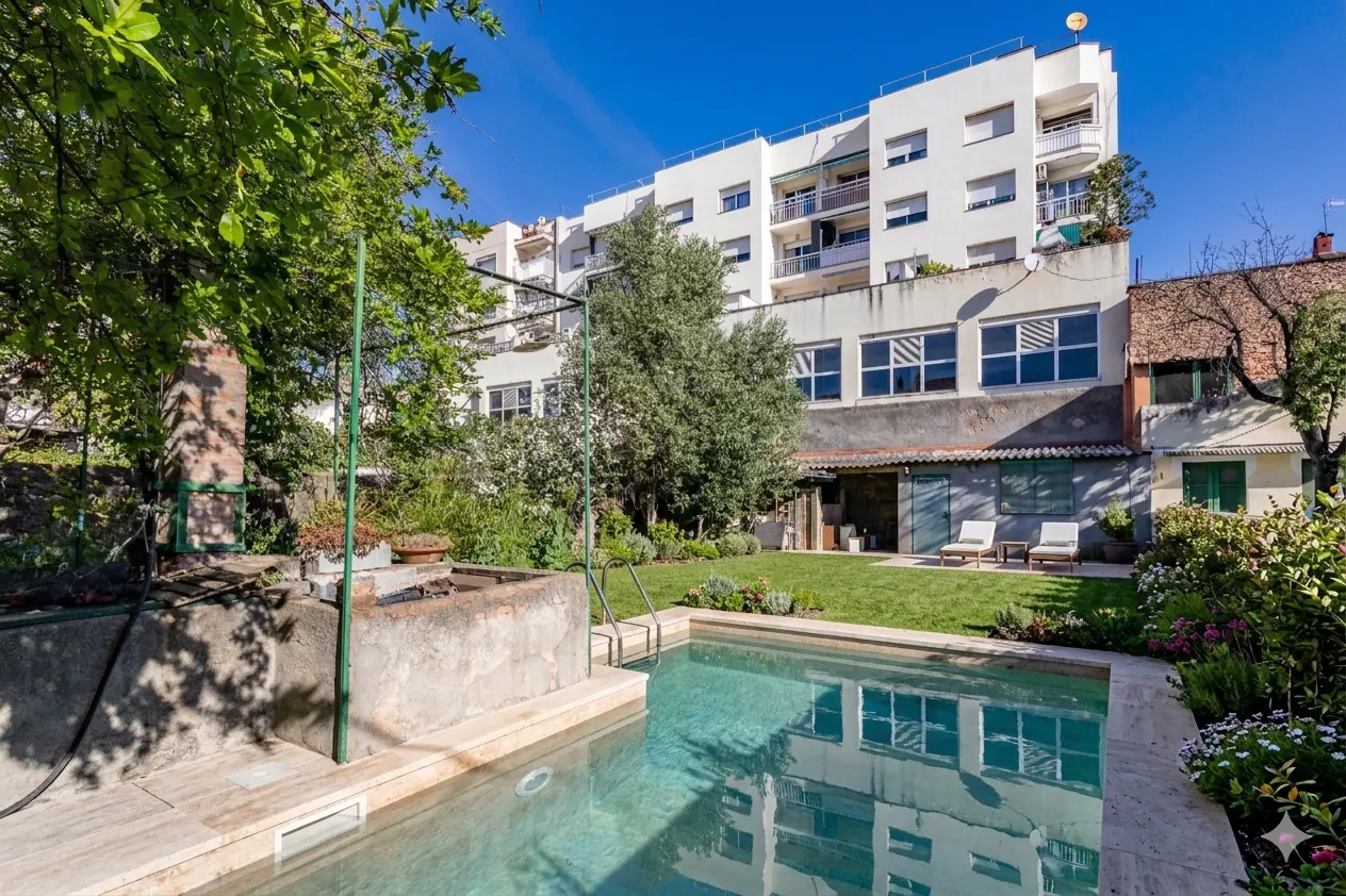 Backyard view of a pool with clear blue water, a green lawn, and a white building in the background.