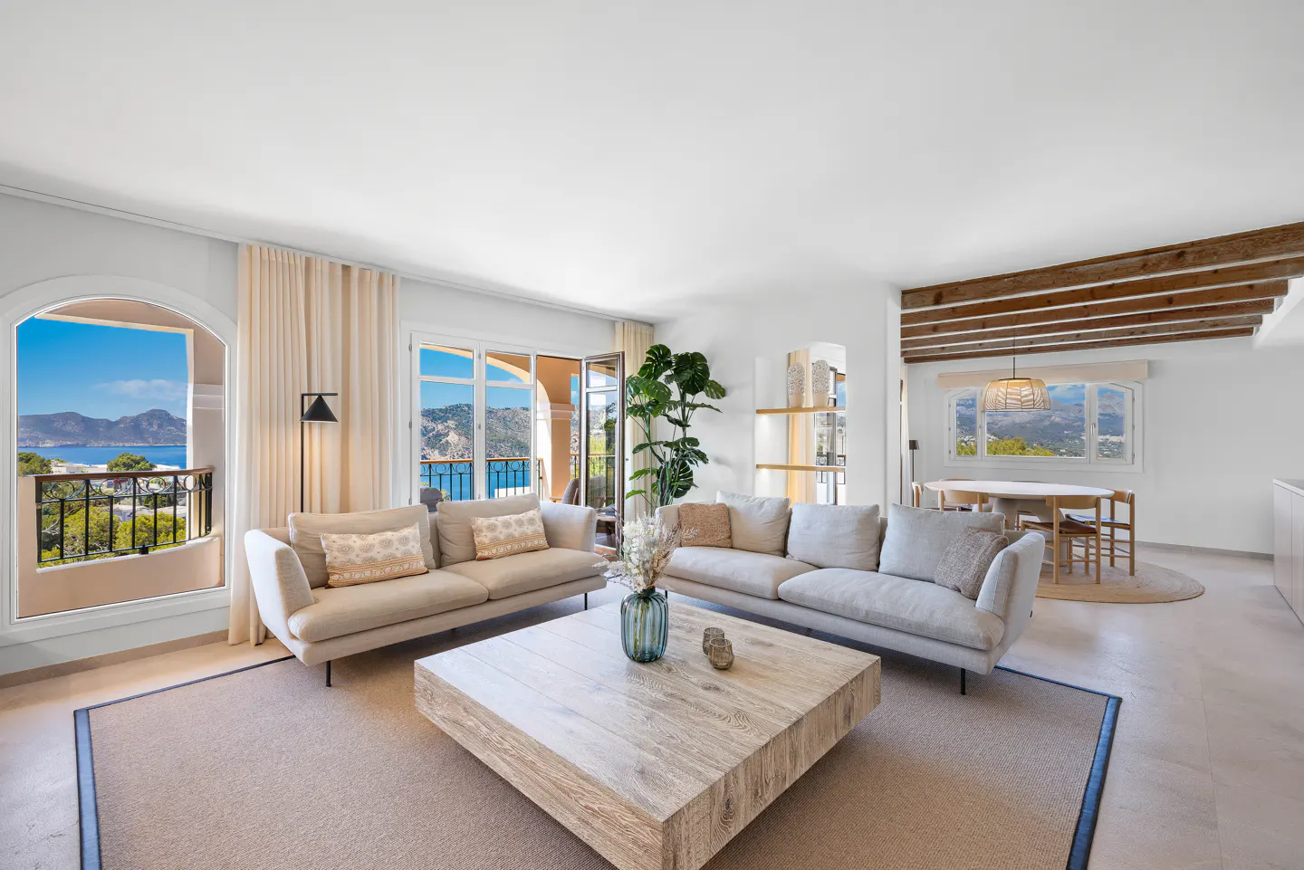 Bright living room with two sofas, a large wooden coffee table, and ocean views from the windows and balcony.