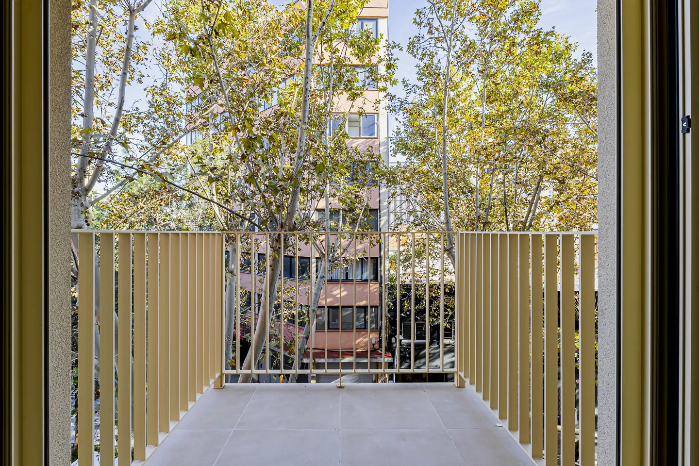 Balcony view with beige railings and tile floor. Trees and a building are visible in the background.