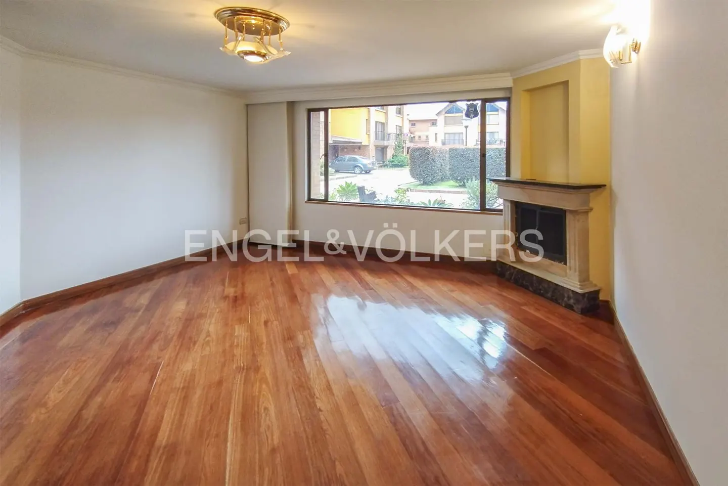 Bright, empty living room with hardwood floors, a stone fireplace, and a large window overlooking a green yard.