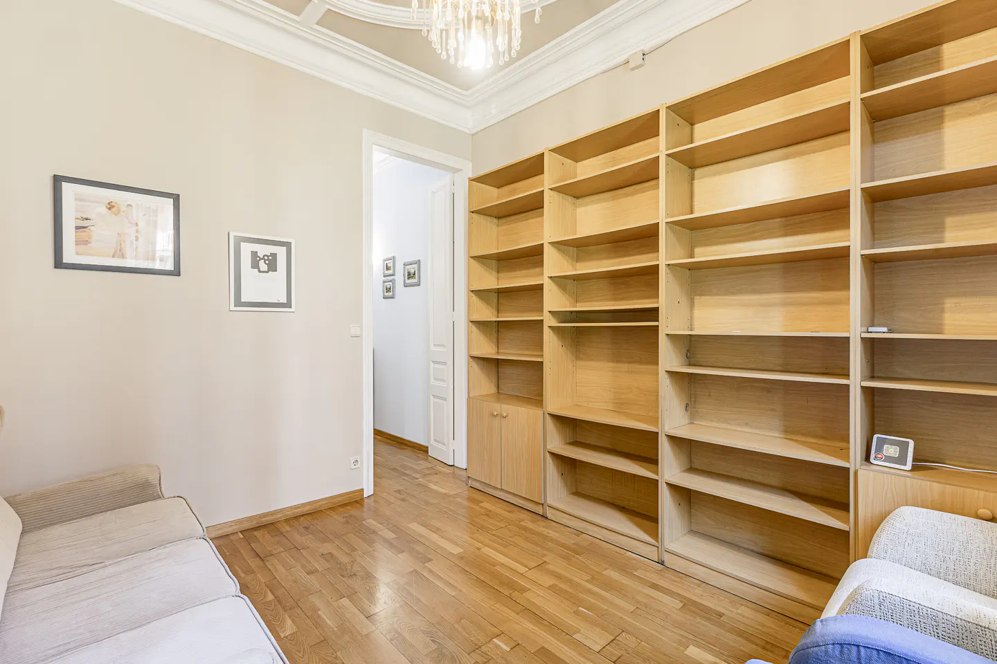 A living room with hardwood floors, a beige sofa, and a large, empty wooden bookshelf.