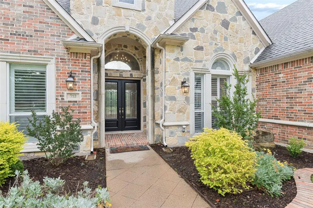 Exterior view of a two-story house with a stone and brick facade, black double doors, and manicured landscaping.