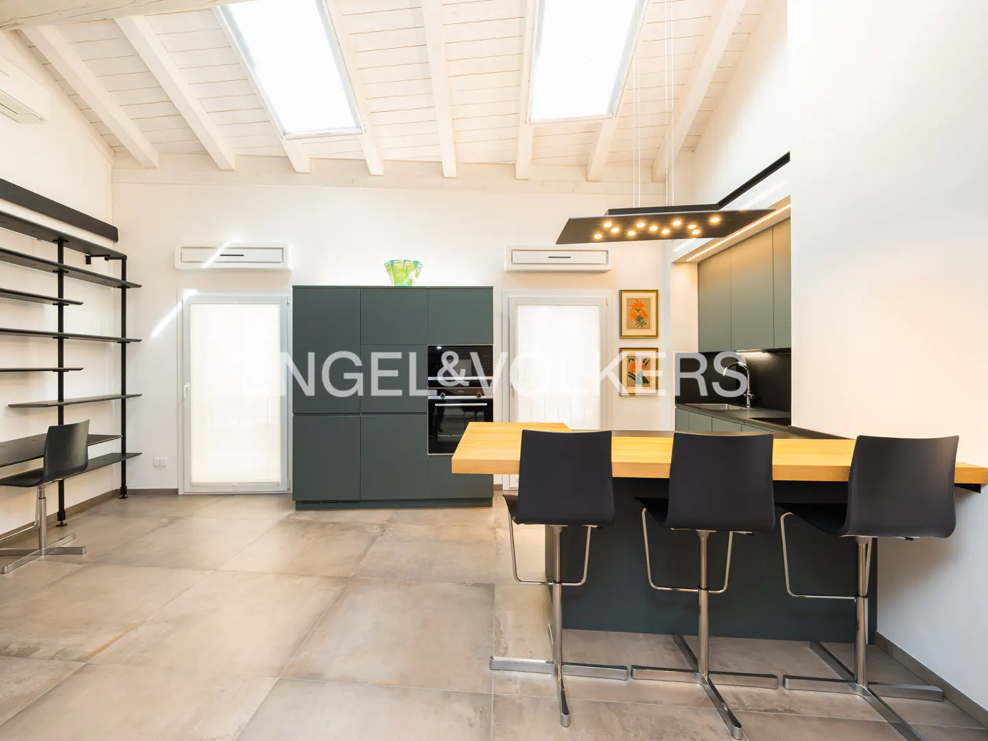 A modern kitchen with gray cabinets, a wooden countertop island with three black chairs, and a black shelving unit.