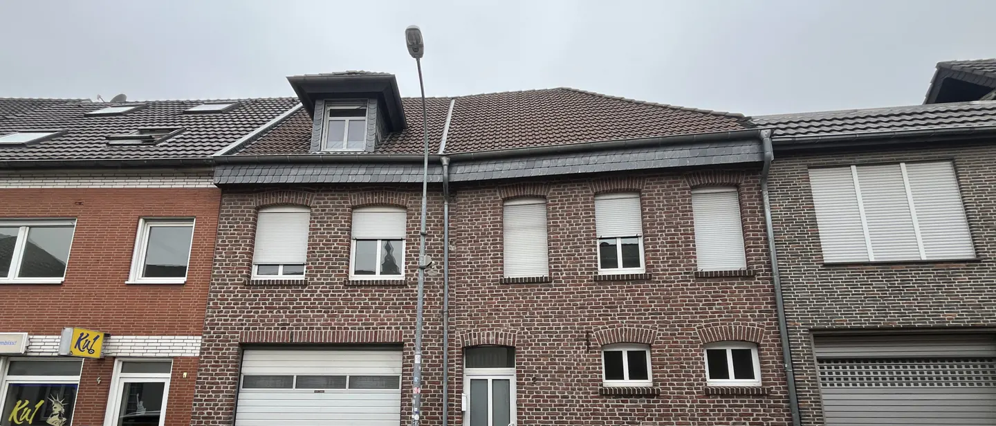 A three-story brick building with white window shutters and a gray roof on a cloudy day.