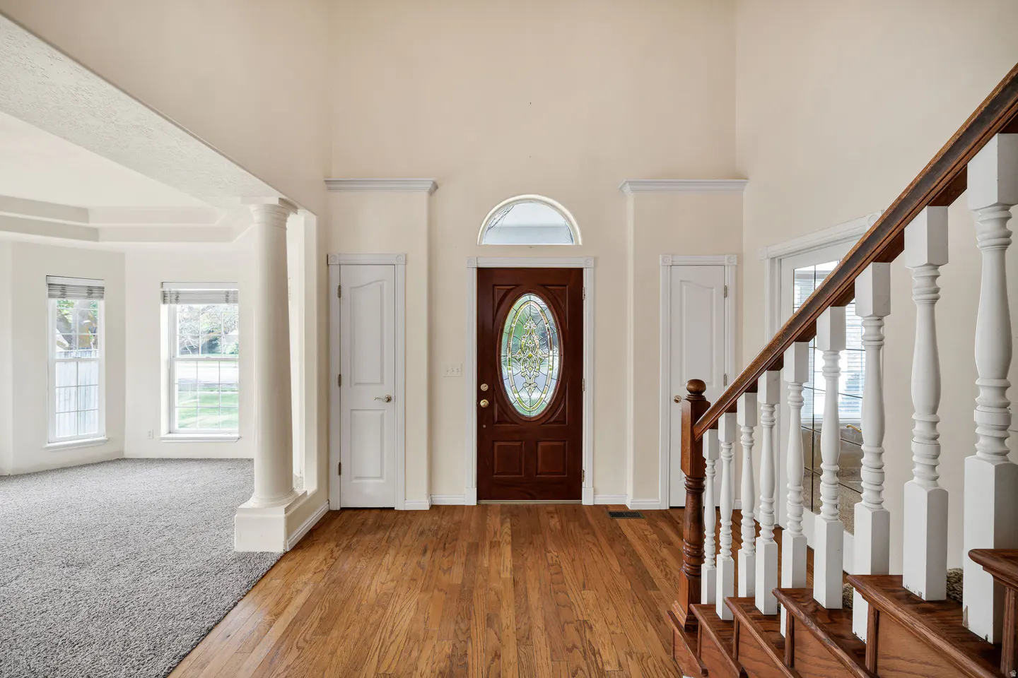 Foyer with hardwood floors, a dark wood front door with oval glass, and a staircase with white spindles.